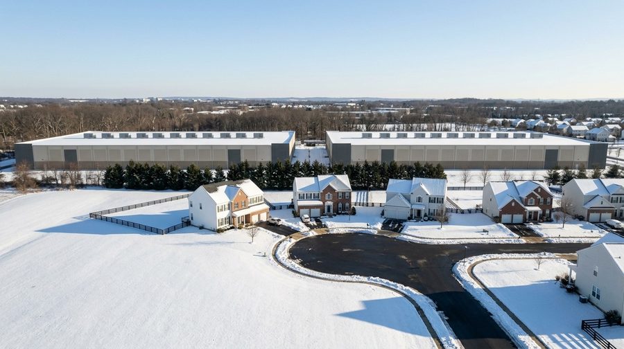 A snowy cul-de-sac of homes with two data center halls past the trees